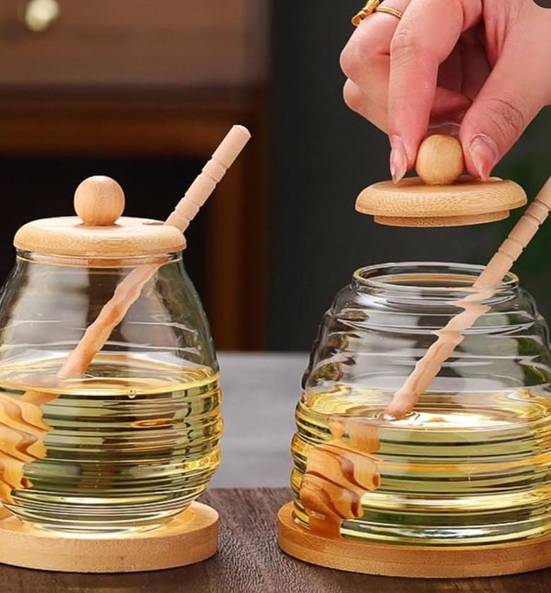 Glass honey jar with wooden lid, stirring stick and base. image